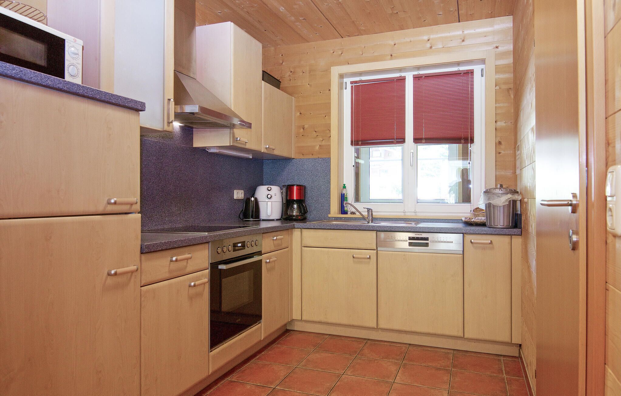 A compact kitchen with wooden cabinets, a built-in oven, a coffee maker, and a window with blinds.