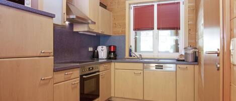 A compact kitchen with wooden cabinets, a built-in oven, a coffee maker, and a window with blinds.
