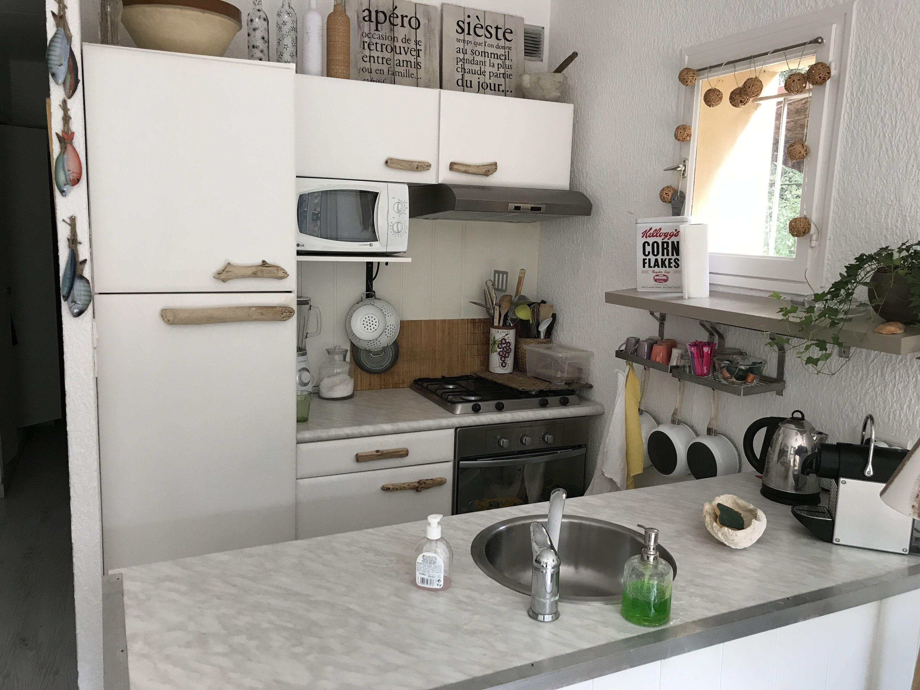Une cuisine avec des meubles blancs, un four à micro-ondes, une cuisinière, un évier et divers ustensiles de cuisine.
