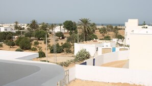 A residential area with white buildings, palm trees, and a clear view of the sea. - VILLA FAMILYA (Djerba Midoun Tezdaine) (DJERBA MIDOUN TEZDAINE)