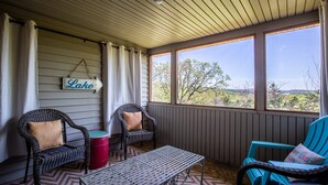 A covered porch with wicker chairs, a metal table, and a view of trees and hills.