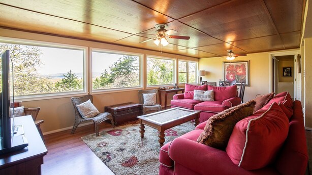 A cozy living room with a large window, a ceiling fan, and a red sofa.