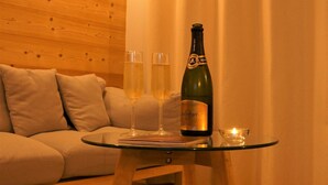 Een gezellige kamer met een houten wand, een glazen tafel met een fles en glazen, en een zacht wit tapijt.