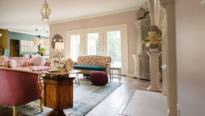 A spacious living room with a large sofa, a coffee table, and a decorative lamp. There is a large window providing natural light and a view of the outdoors. - Close to BROADWAY BNA-Gorgeous Home - Idyllic Countryside, Heated Pool & Hot Tub (Mt Juliet)