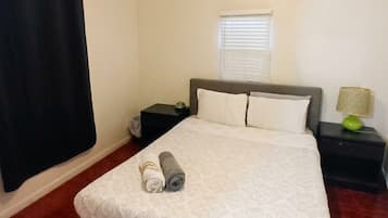 A bedroom with a bed, a ceiling fan, a window with blinds, and a nightstand with a lamp.