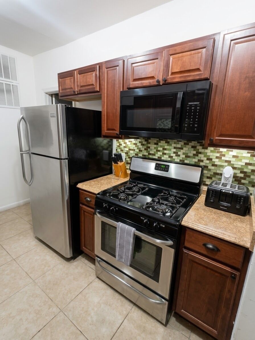 A kitchen with stainless steel appliances, wooden cabinets, and a tiled backsplash.