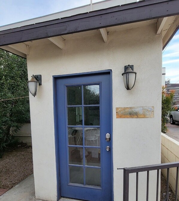 A building with a blue door, two wall-mounted light fixtures, and a small sign on the wall.