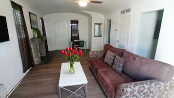A living room with a white coffee table, a brown patterned sofa, and a vase of red flowers.