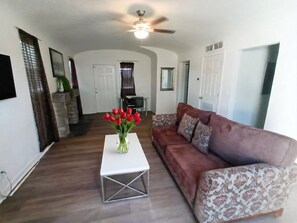 A living room with a white coffee table, a brown patterned sofa, and a vase of red flowers.