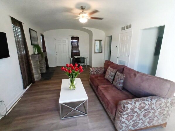 A living room with a white coffee table, a brown patterned sofa, and a vase of red flowers.