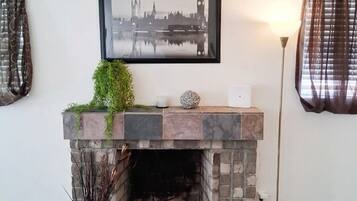 A fireplace with a stone mantel, a framed picture above it, and a potted plant beside it.