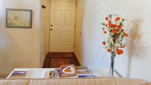A hallway with a white door, a framed picture on the wall, and a table with brochures and a vase of flowers. - Artist Retreat in the Heart of Plaza (Taos)