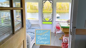 Interior acogedor de una cabaña con vista a un lago, un sofá a rayas, una mesa de comedor y una puerta decorativa.