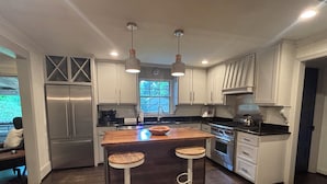 Una cocina moderna con electrodomésticos de acero inoxidable, una isla de madera con taburetes altos y armarios blancos.