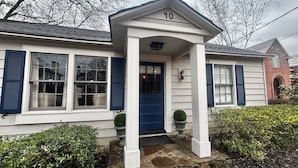 Una casa con puerta principal azul, revestimiento blanco y contraventanas azules.