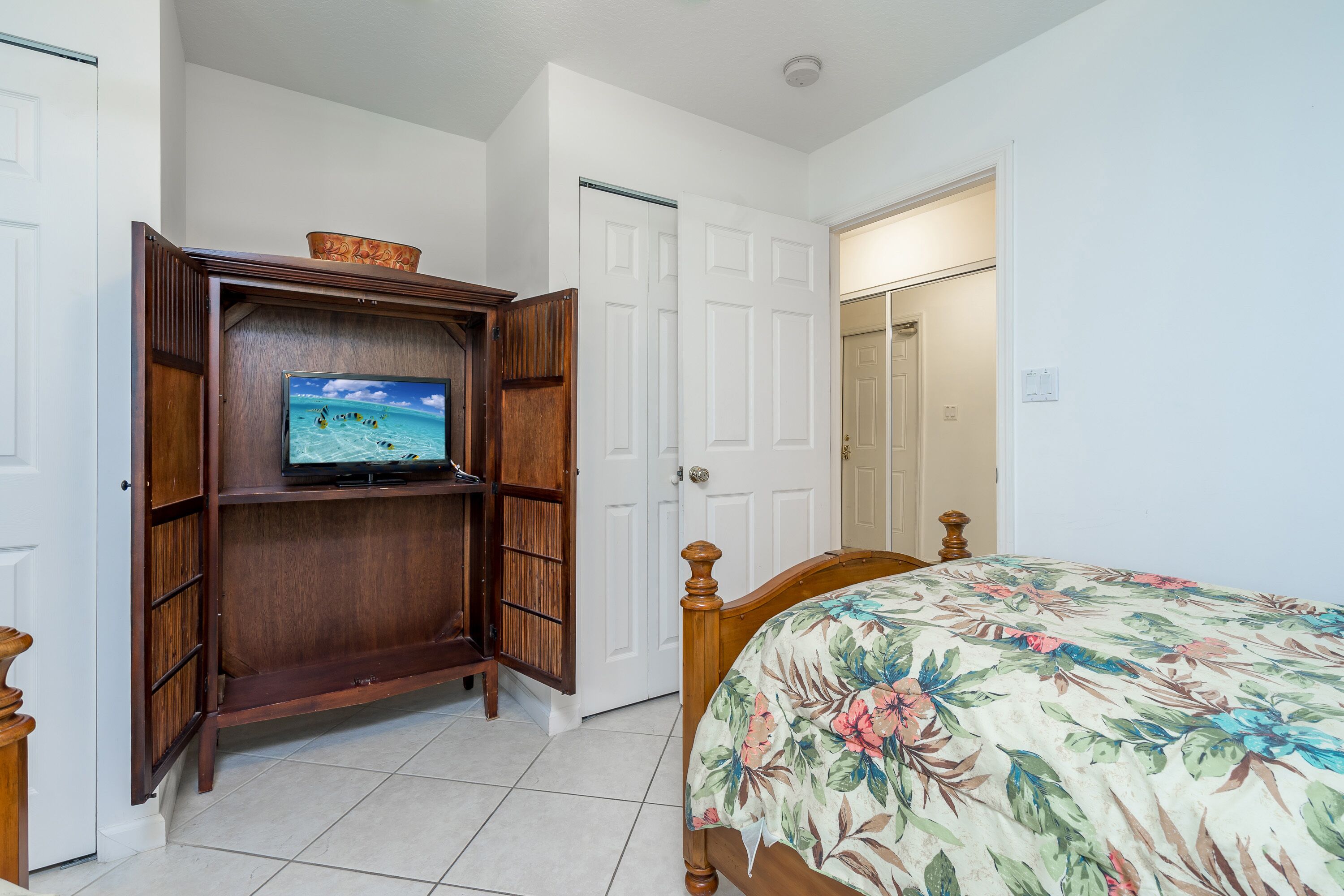 Ein Schlafzimmer mit einem Bett, einem Holzschrank mit Fernseher und weißen Türen.