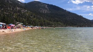 A beach with clear water, tents, and a mountainous backdrop. - Lake & Mountain Views Condo - 5 min. drive to lake, ski and golf (Incline Village)