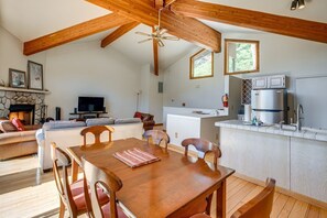 Un vaste espace de vie comprenant une table à manger en bois, des canapés, une cheminée, un téléviseur et une cuisine équipée d’un réfrigérateur et d’un évier.