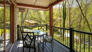 Una terrazza coperta all'aperto con tavolo e sedie, circondata da una ringhiera in legno e con vista su una zona boschiva.