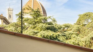 A table with a bottle of wine and a vase of flowers, overlooking a cityscape with a prominent dome and tower. - Amazing Penthouse Le Terrazze Luxury Apartment Duomo view (Firenze)