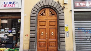 A wooden double door with a decorative arch above it, flanked by two storefronts with signs advertising market and bread & wine. - Amazing Penthouse Le Terrazze Luxury Apartment Duomo view (Firenze)