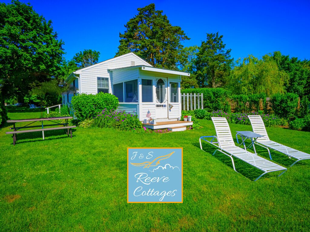 A white cottage with a porch, surrounded by a well-maintained lawn and a wooden fence.