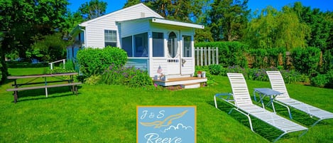 A white cottage with a porch, surrounded by a well-maintained lawn and a wooden fence.