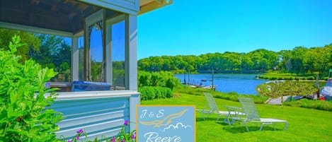 Een vakantiehuisje aan het meer met een overdekte veranda, een bordje met J&S Reeves Cottages en een gazon met lounge fauteuils.