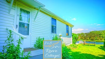 A white cottage with a porch, surrounded by greenery and a clear sky.