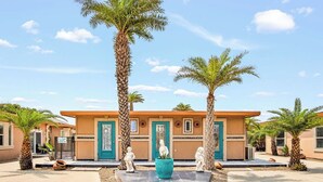 A building with a beige facade, multiple doors, and palm trees in the foreground.
