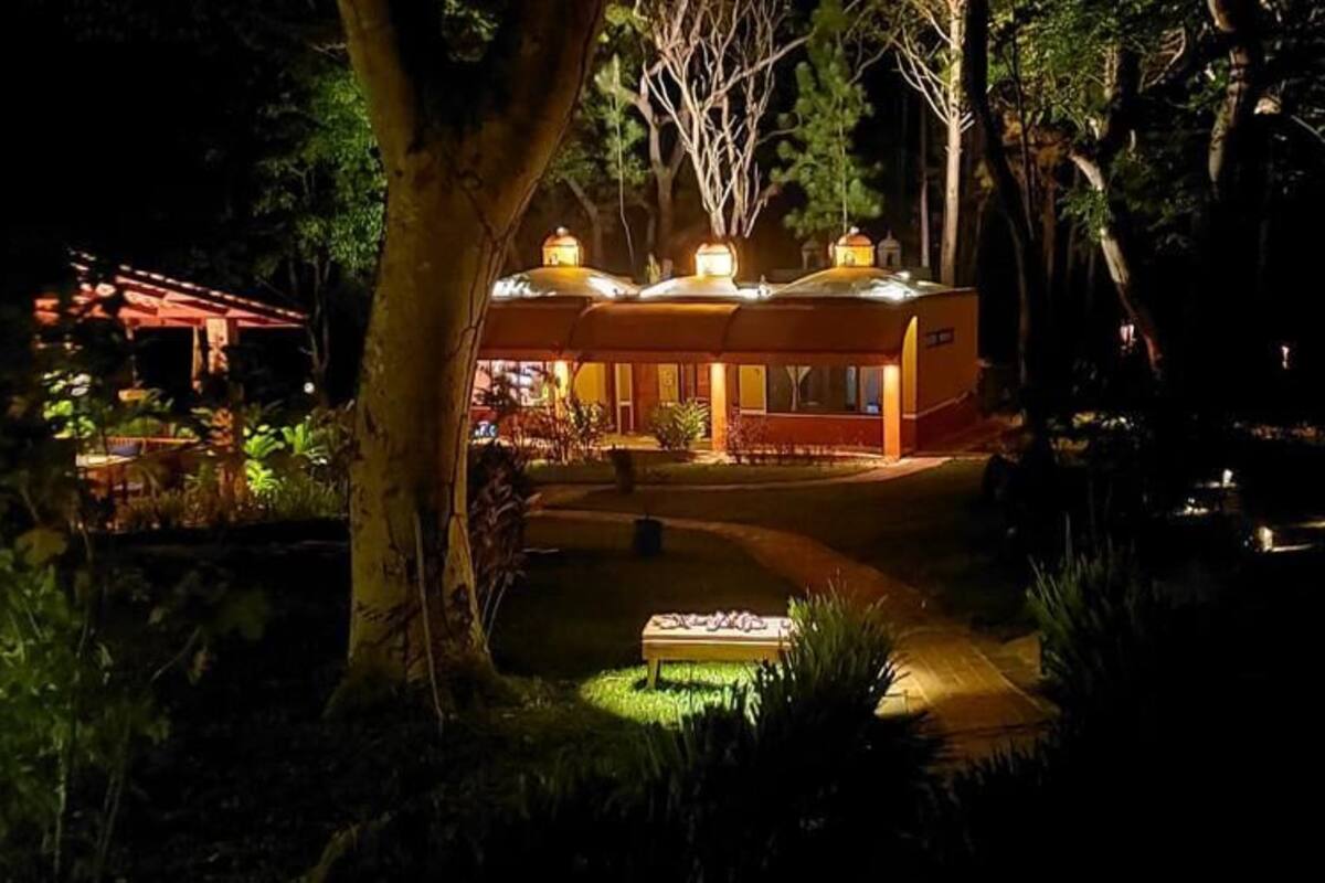 A modern building with a curved roof, surrounded by lush greenery and a well-lit pathway leading to it.