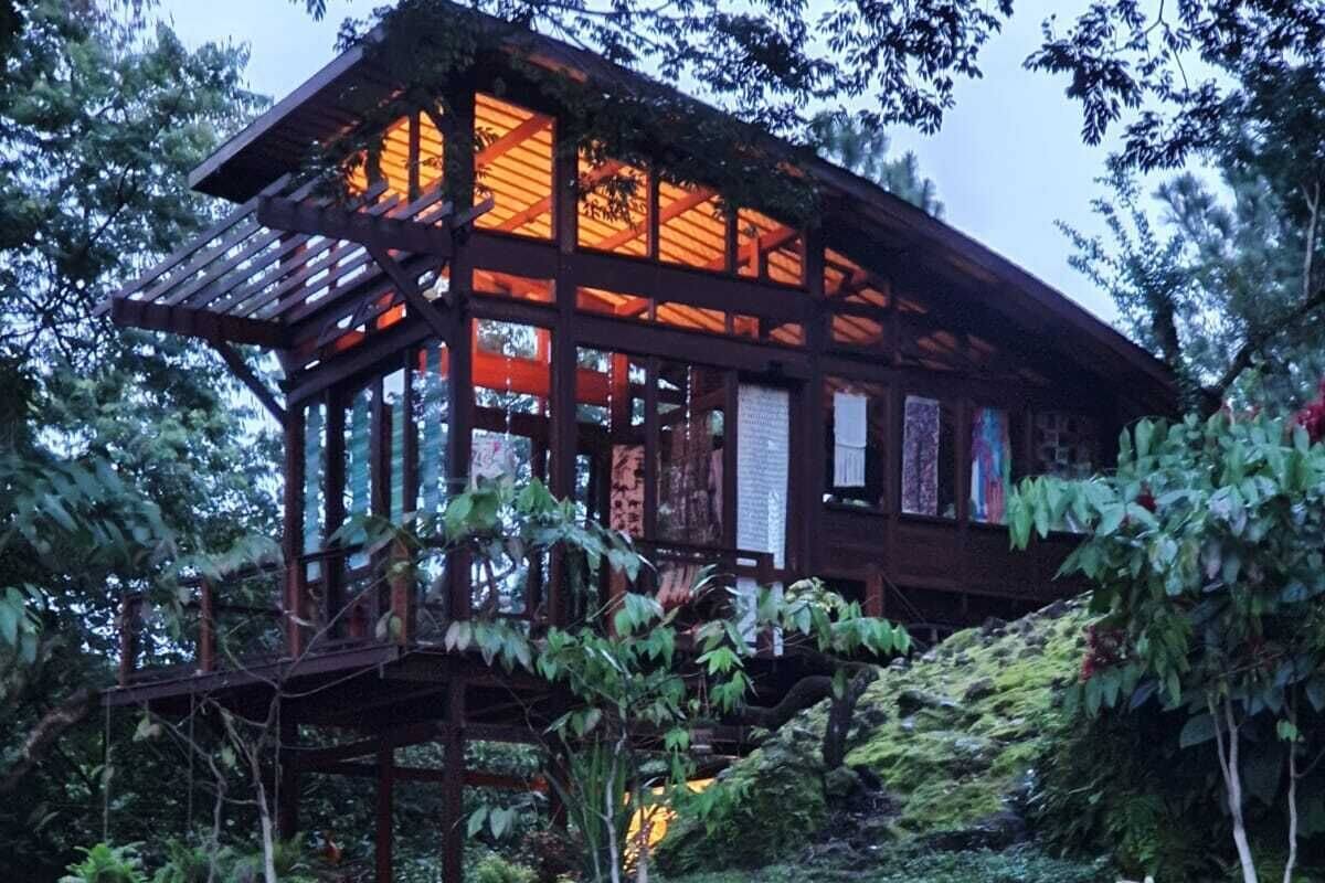 A wooden house with a glass facade, surrounded by a landscaped garden with a brick pathway.