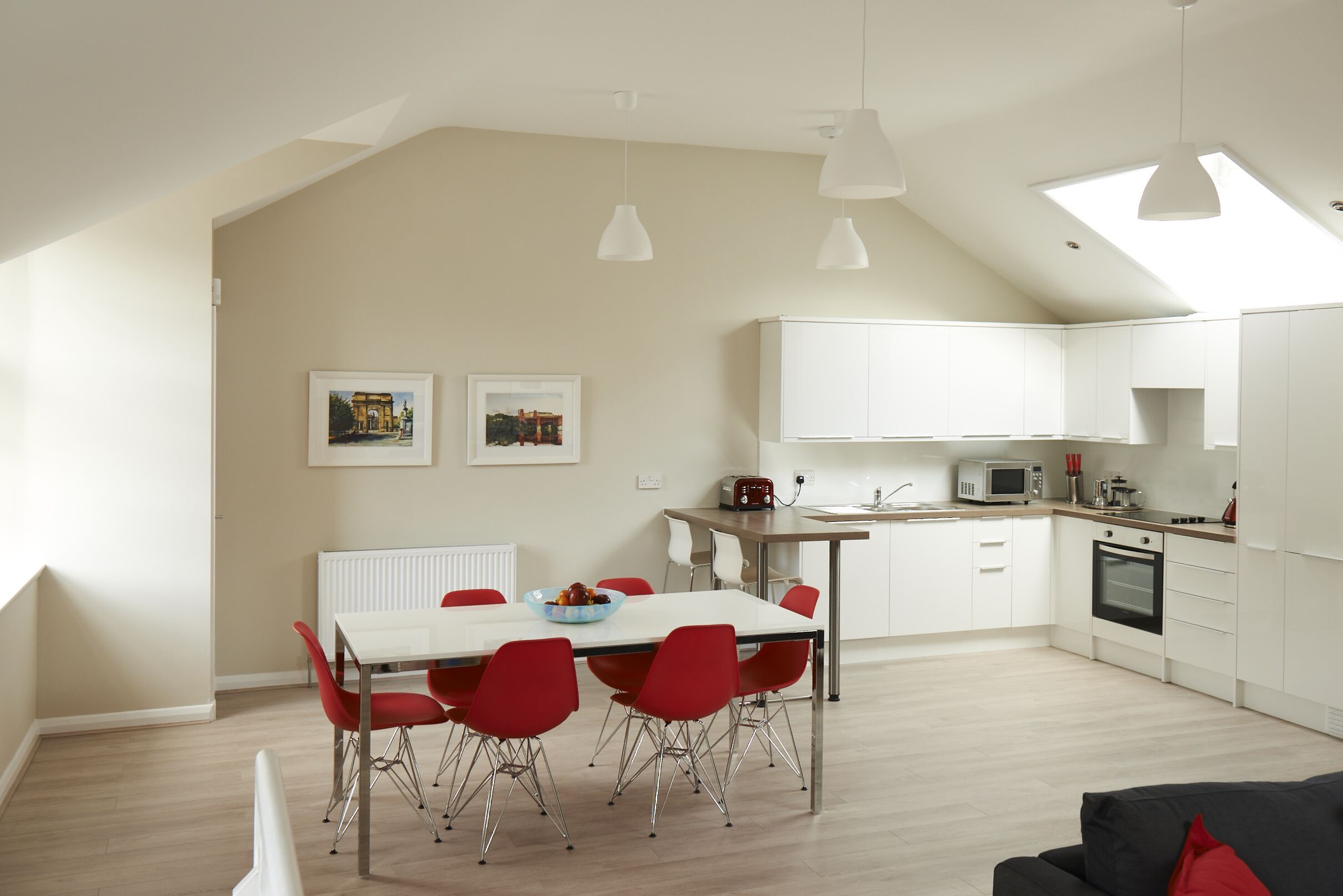 A modern kitchen with white cabinets, a dining table with red chairs, and a black oven.