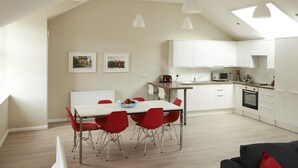 Una cocina moderna con armarios blancos, una mesa de comedor con sillas rojas y un horno negro.