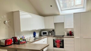 Una cocina moderna con armarios blancos, microondas, tostadora y tetera roja.