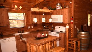 Cocina de cabaña de madera con una isla central, taburetes de madera, estufa, lavabo y refrigerador.