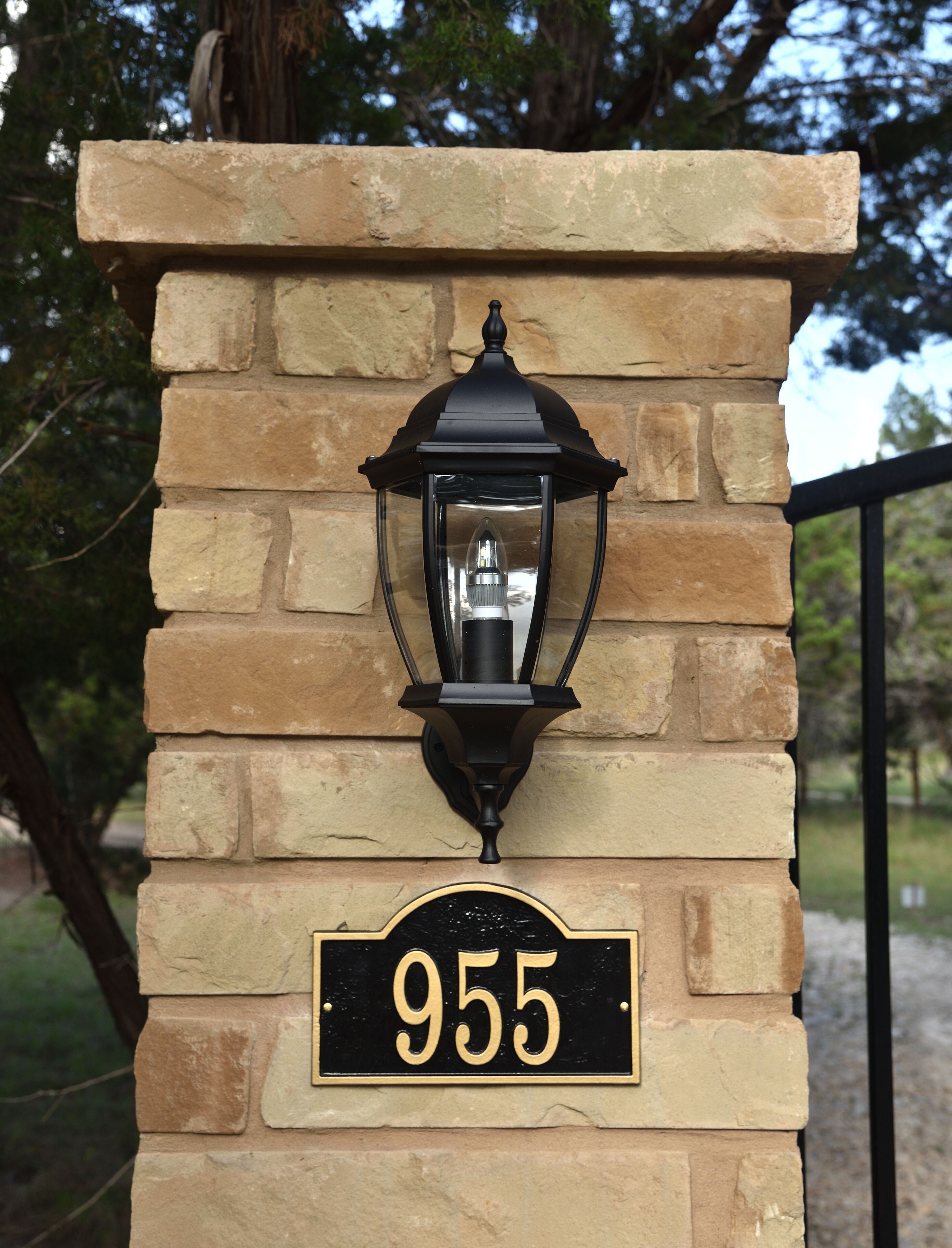 Un mur de pierres sur lequel est fixée une lanterne noire et une plaque noire portant le numéro 955.