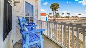 Un portico con due poltrone Adirondack blu, una ringhiera bianca e vista su palme e case.