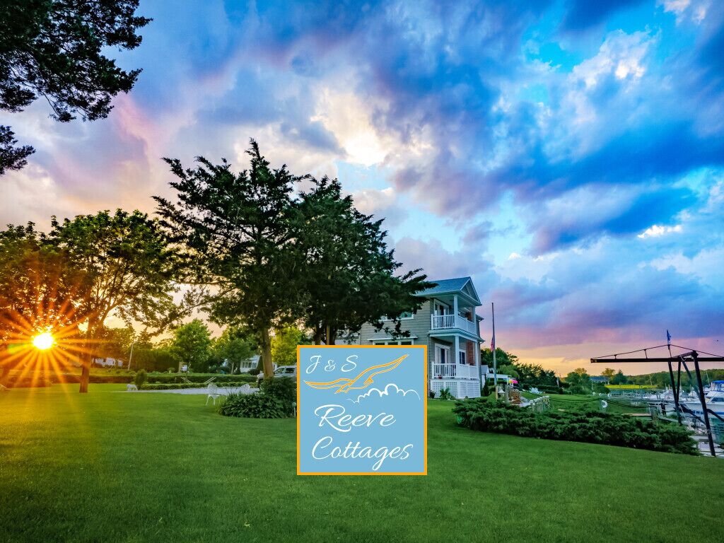 A sign for J&S Reeves Cottages with a view of a house and trees.