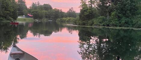 A dock with kayaks and a rowboat, surrounded by trees and a calm lake.