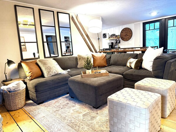 A modern living room with a sectional sofa, ottomans, a coffee table, and a large mirror.