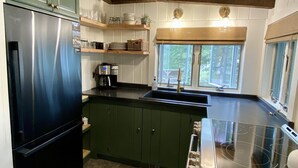 Una cocina con gabinetes verdes, un refrigerador de acero inoxidable, una estufa integrada y un ventanal con vistas a árboles.