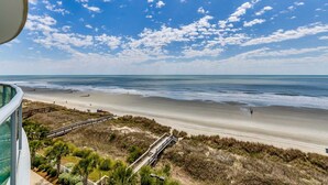 A beach view with a clear sky, a sandy shore, and a wooden boardwalk leading to the beach. - 6th Floor, Beachfront. Sundeck, Lazy River, Kiddie Pools | Bluewater Keyes - 606 (North Myrtle Beach)