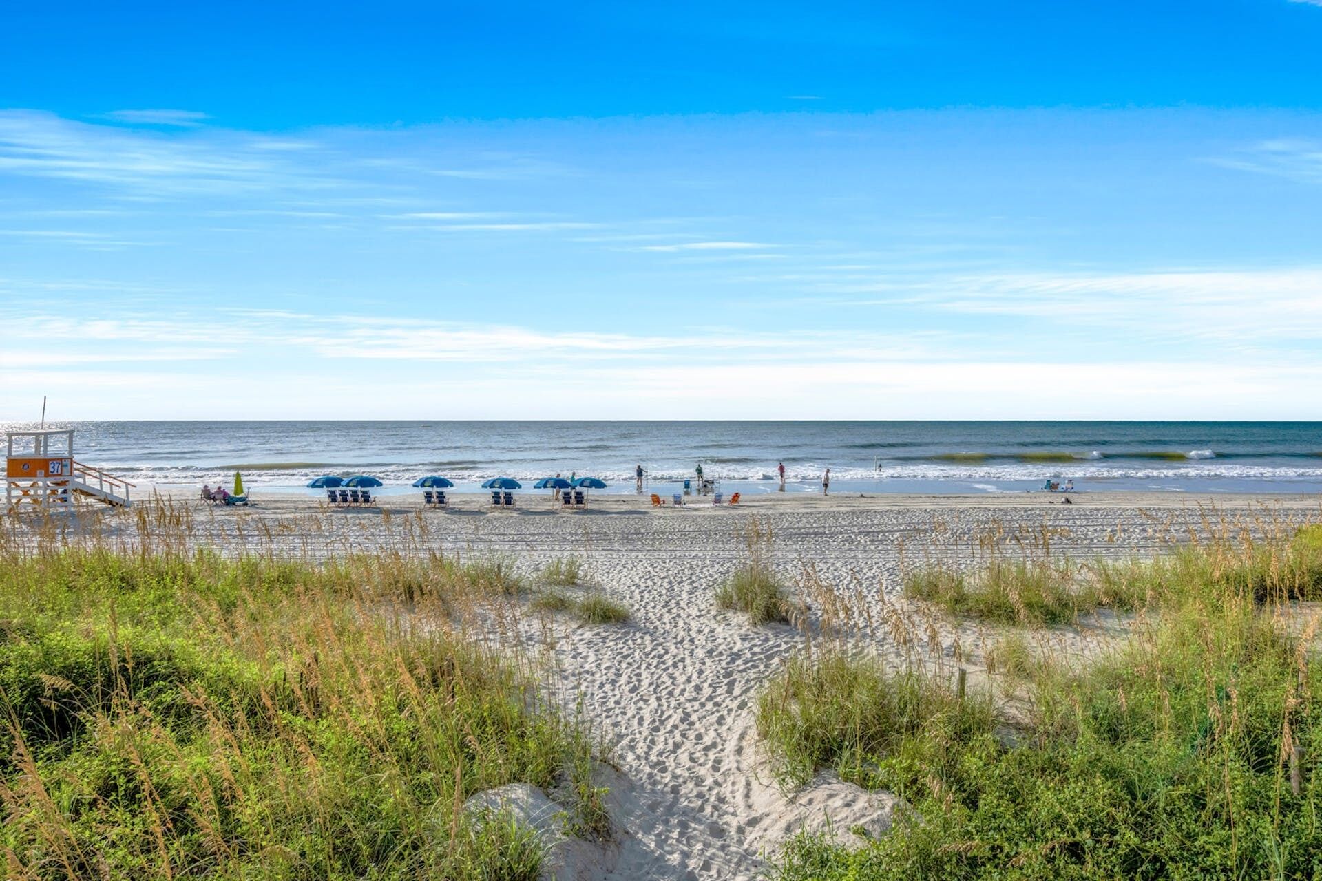 A beach with a lifeguard tower, beach umbrellas, and people enjoying the shore.