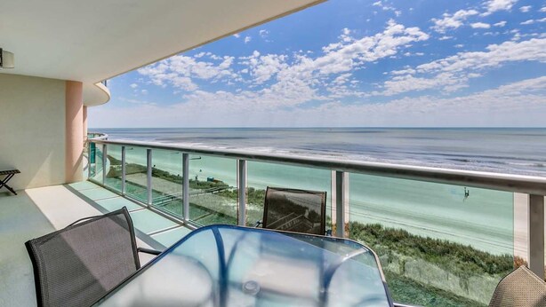 A balcony with a glass railing overlooking a beach and ocean. - 6th Floor, Beachfront. Sundeck, Lazy River, Kiddie Pools | Bluewater Keyes - 606 (North Myrtle Beach)