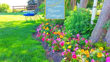 Un jardin agrémenté d’une pancarte indiquant « J&S Reeves Cottages », entouré de fleurs aux couleurs vives et délimité par une clôture en bois.