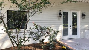 A white house with a covered porch, a small garden with yellow flowers, and a window with a black frame.