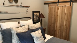 A bedroom with a bed, pillows, a lamp, a picture frame, and a wooden door.