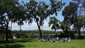 An outdoor seating area with green chairs and a small table, surrounded by trees with Spanish moss.