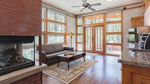 A spacious living area with a fireplace, a sofa, a coffee table, and a large window offering a view of the outdoors.